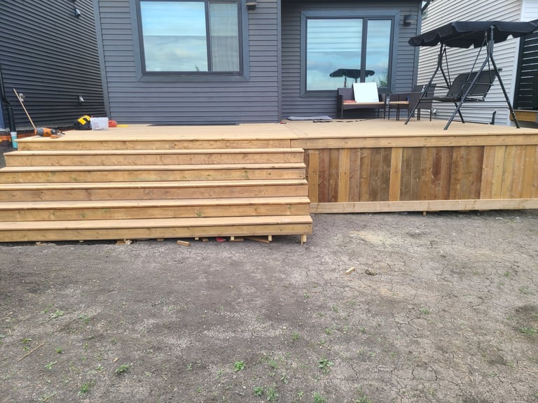 Wooden deck under construction with unfinished planks in a backyard next to a gray house with windows