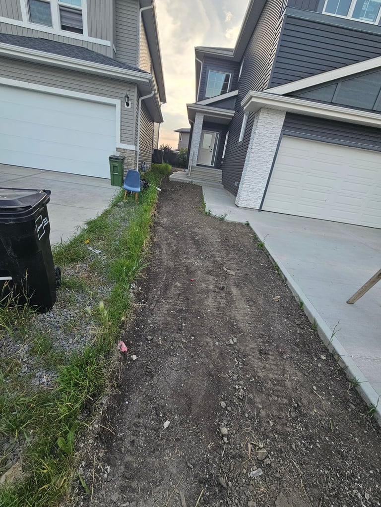 Narrow gravel pathway between two houses with white garage doors and gray siding