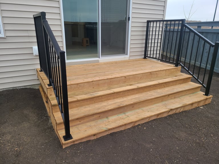 Wooden elevated deck with black metal railings and steps, attached to a house with sliding glass doors