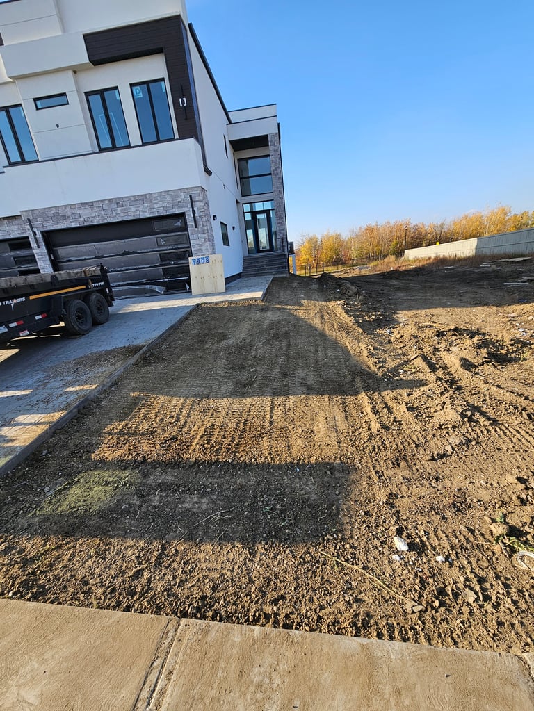 Modern house with attached garage and truck parked on construction site with dirt pile and bare trees in background